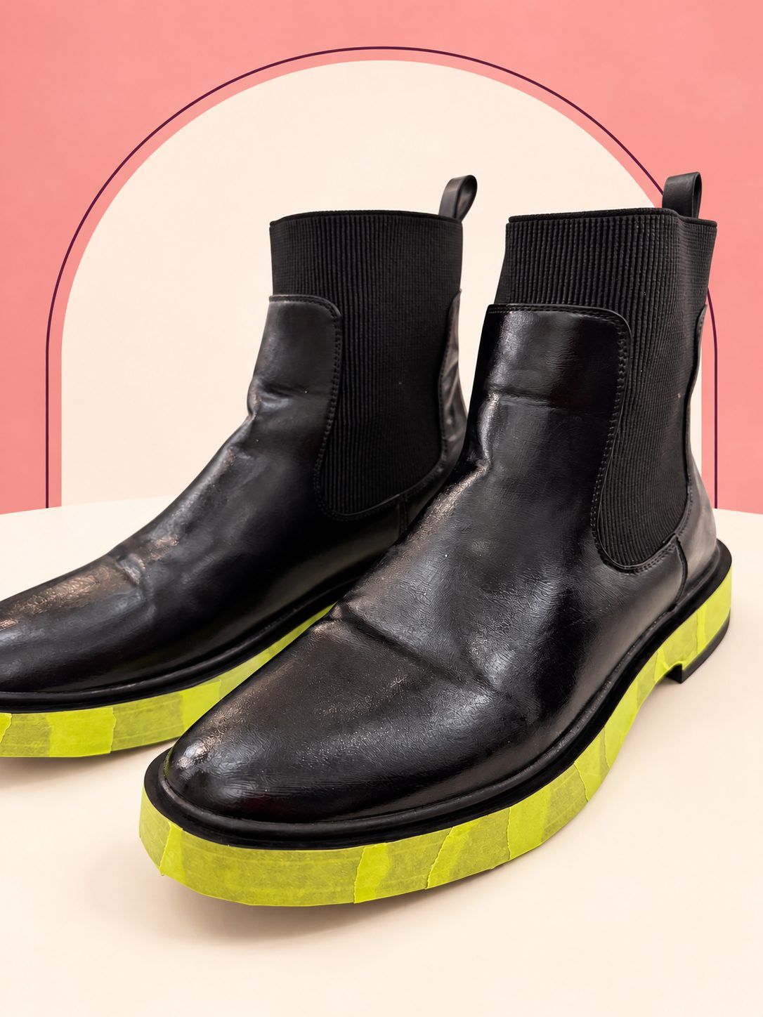 Black ankle boots prepared for gilding, with masking tape protecting the soles.